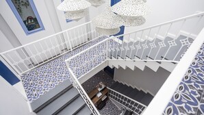 A multi-level interior with a patterned floor, white railings, and hanging white lanterns. - Sardunya Otel (Bozcaada)