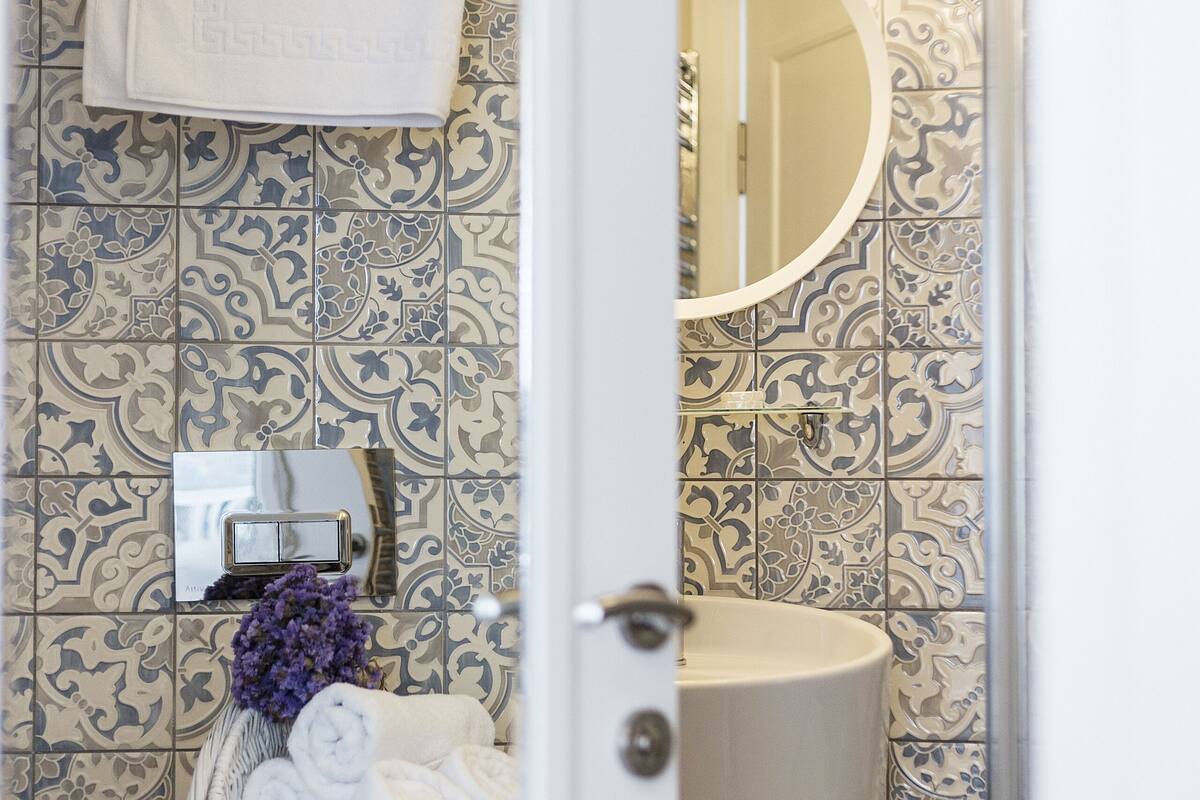 A bathroom with patterned tiles, a white toilet, a wicker basket with towels, and a mirror.