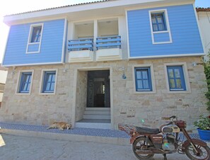 A two-story building with a stone facade and blue trim. - Sardunya Otel (Bozcaada)