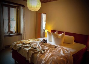 A neatly made bed with pillows and a blanket, a bedside lamp, and a window with curtains.
