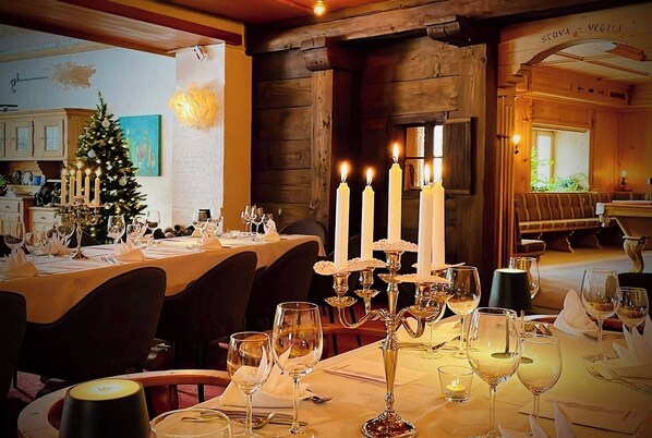 A warmly lit dining area with tables set for a meal, a Christmas tree, and candles.