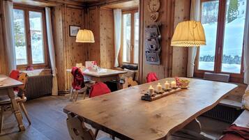 Interior de una cabaña de madera con una gran mesa de comedor, varias sillas y una lámpara colgante.