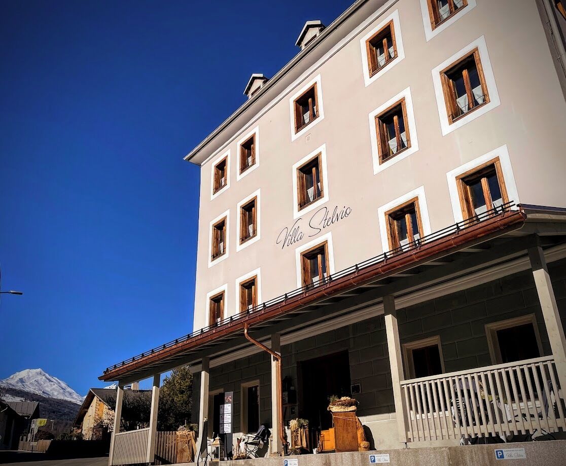 A multi-story building with a sign reading "Villa Stelvio" and a covered entrance area with outdoor seating.