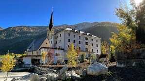 A building with a prominent tower, surrounded by trees and mountains. - Villa Stelvio Bed & Breakfast (Val Muestair)