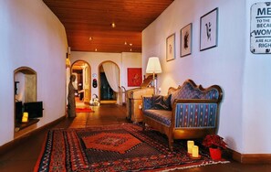 A hallway with a wooden ceiling, a patterned rug, a sofa with a patterned cushion, and a wall-mounted sign.