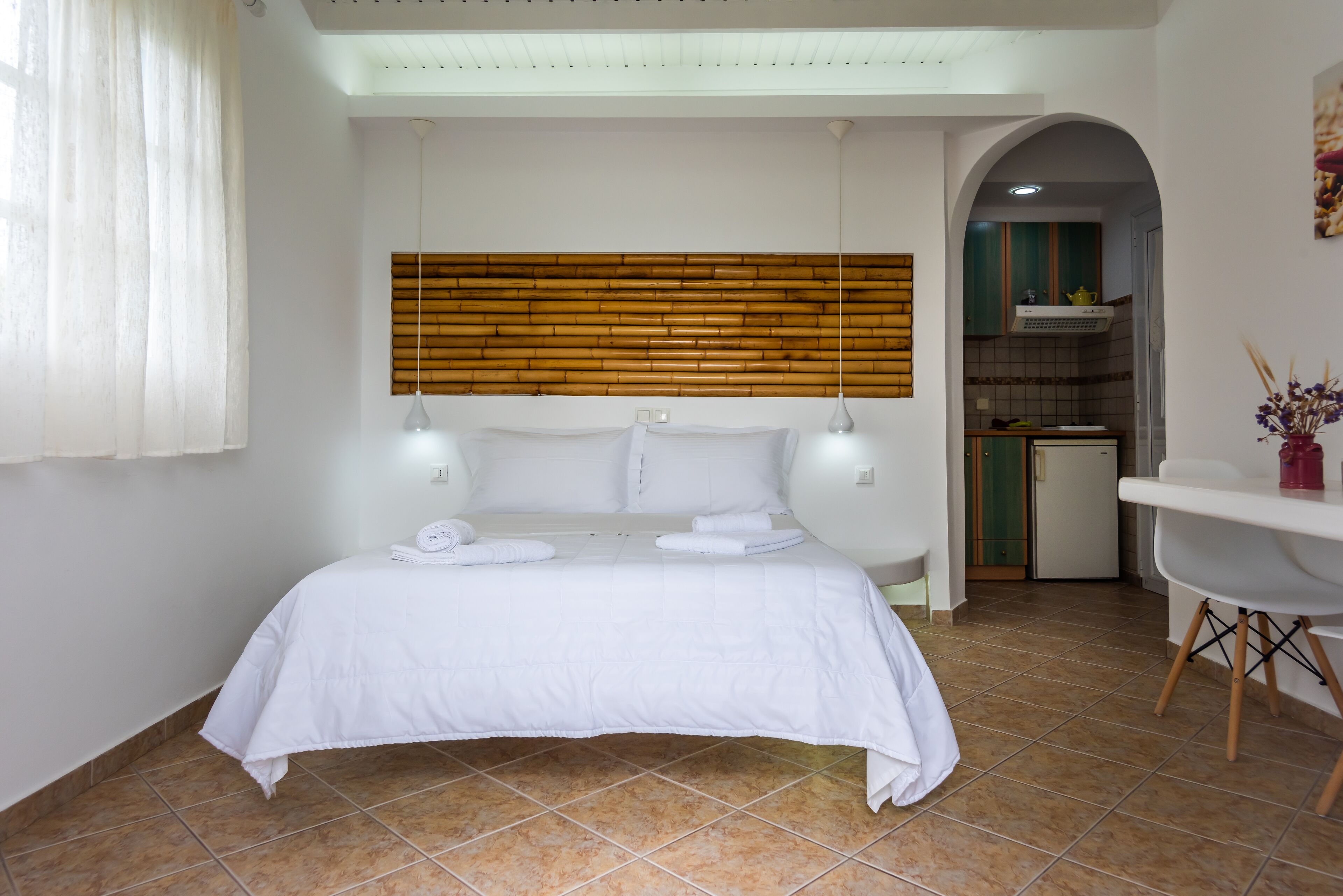 Habitación de hotel con cama, cabecera de madera, mesa de comedor y zona de cocina.