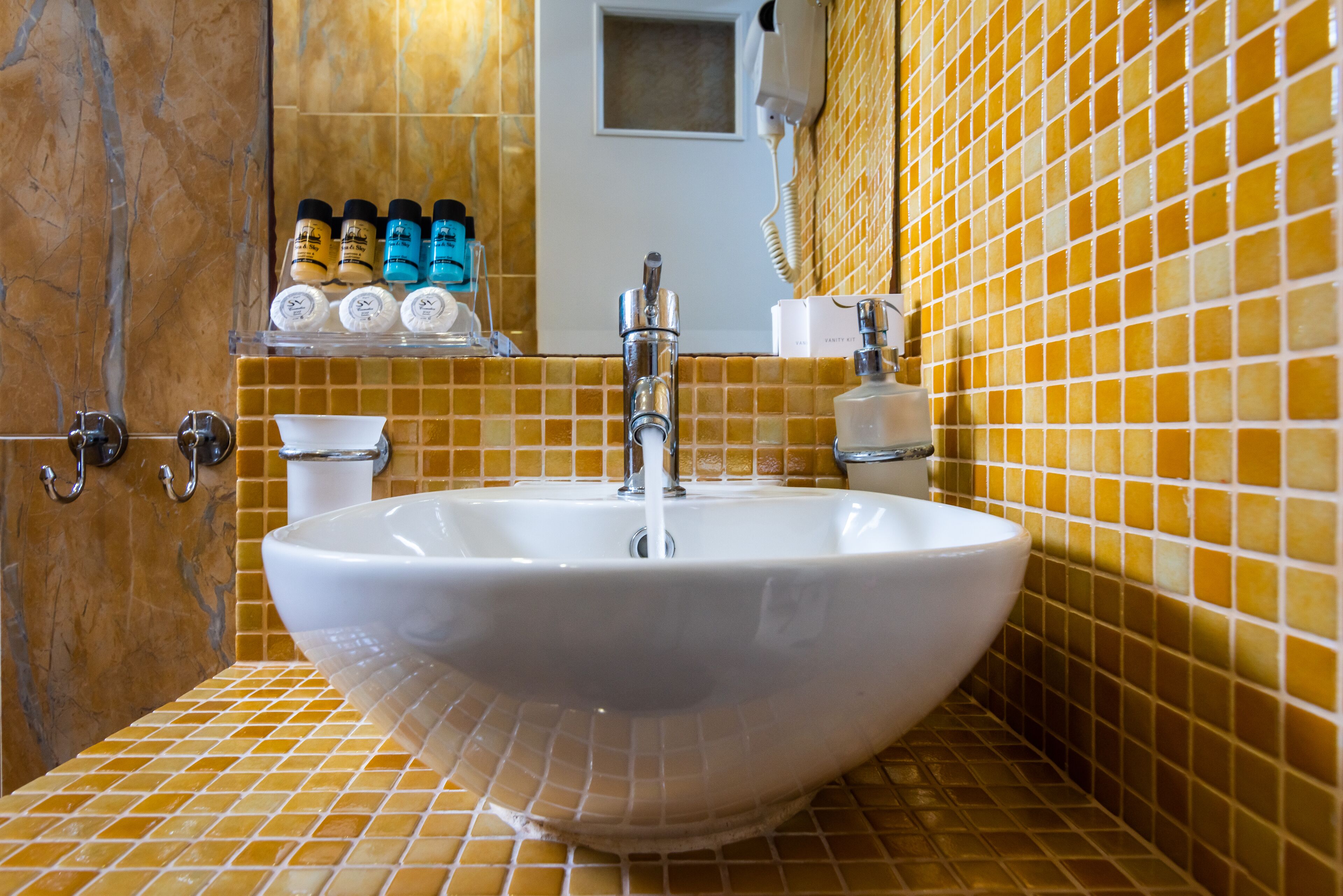 A bathroom with a large white sink, yellow-tiled walls, and a shelf with toiletries.