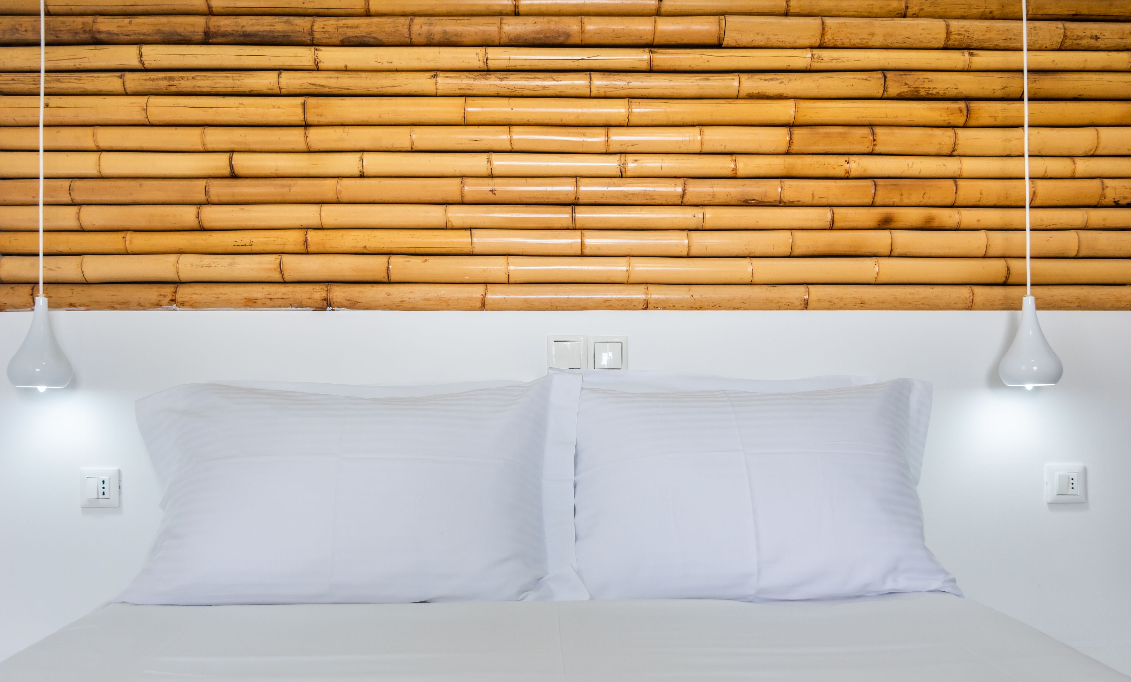 A bed with white bedding, two bedside lamps, and a bamboo headboard.