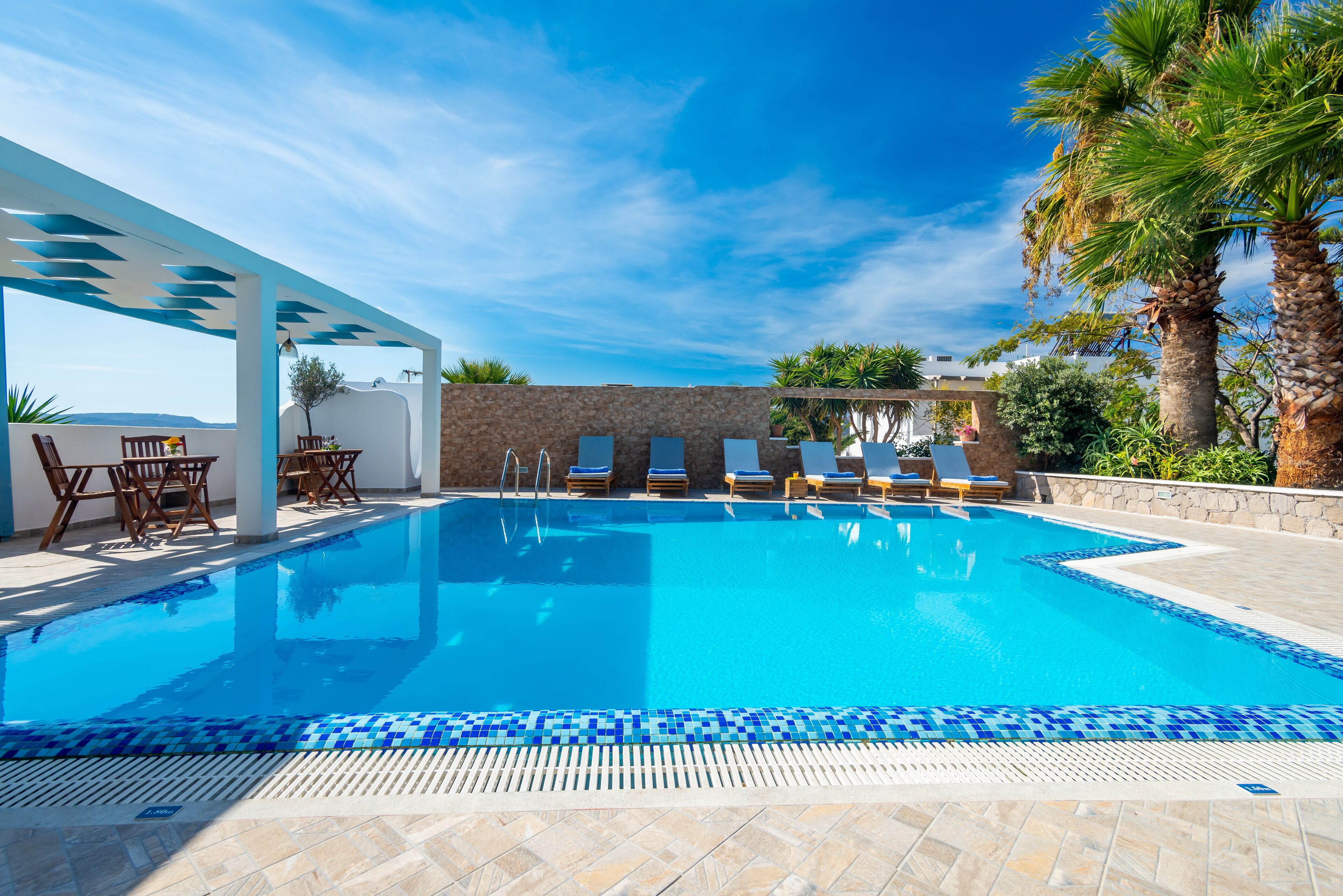 Una piscina azul cristalina con sillas de descanso y un área de estar techada.