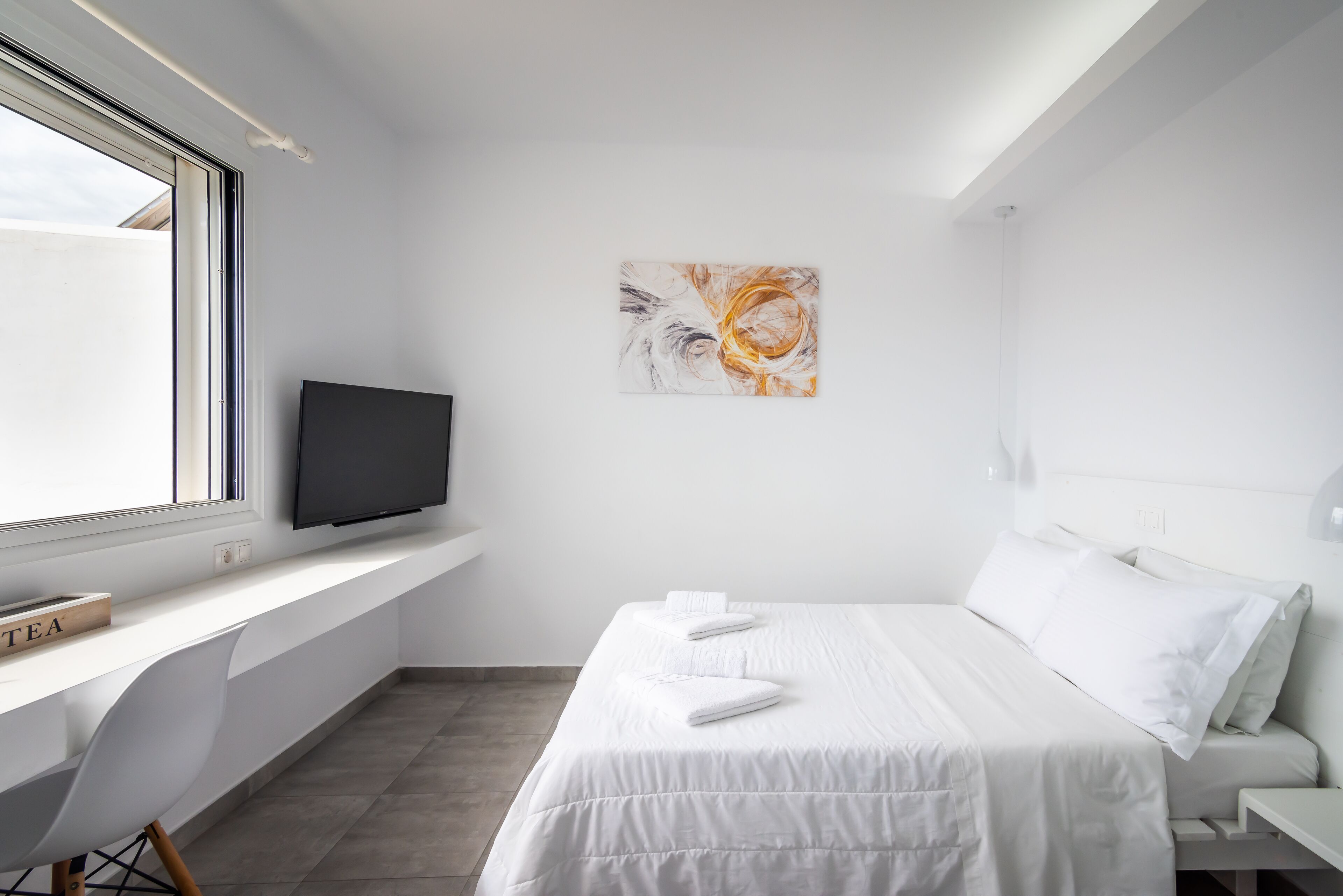 A modern, minimalist bedroom with a bed, a TV on a built-in shelf, and a window.