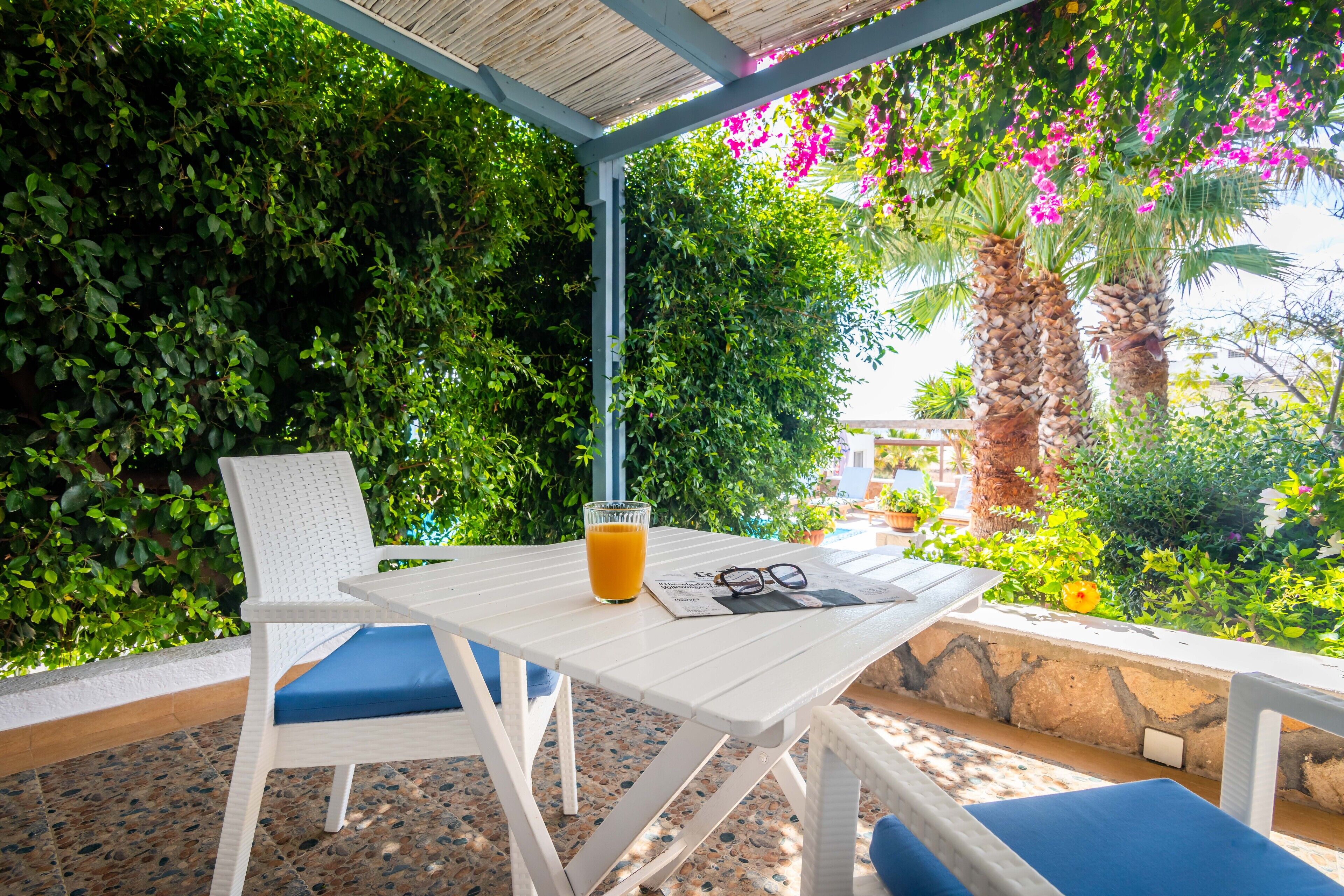 A white table with a blue cushion, a glass of orange juice, and a pair of glasses on it.