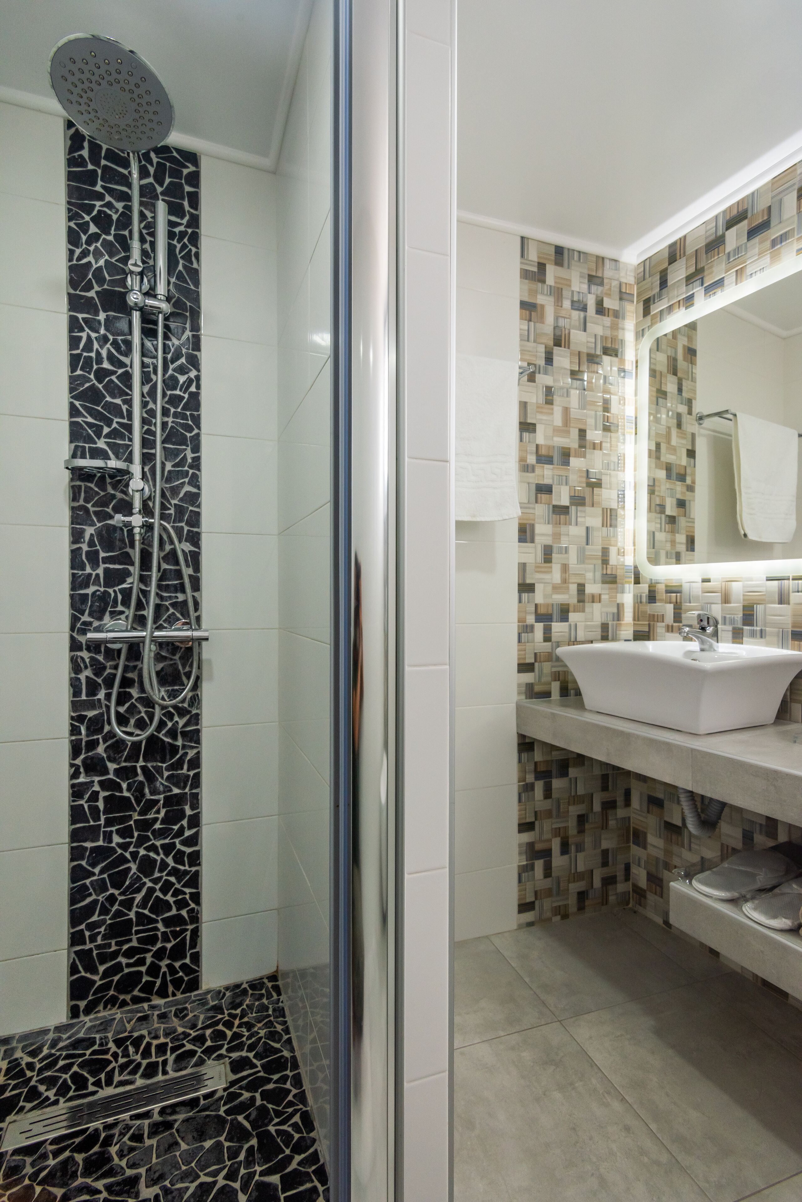 Een badkamer met een douche, een wastafel en een betegelde spatwand.
