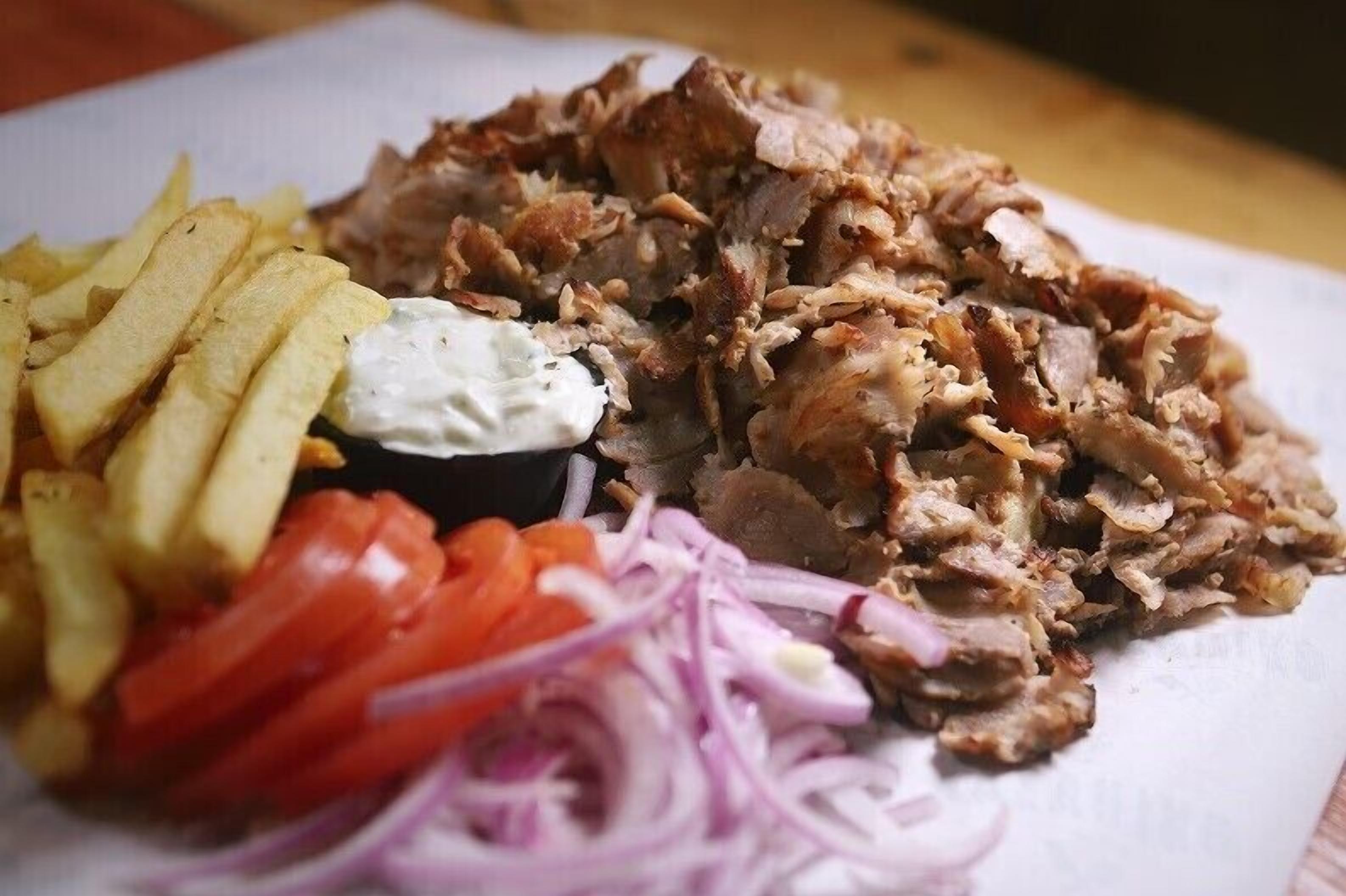 A plate of pulled pork with French fries, sliced tomatoes, and red onions.