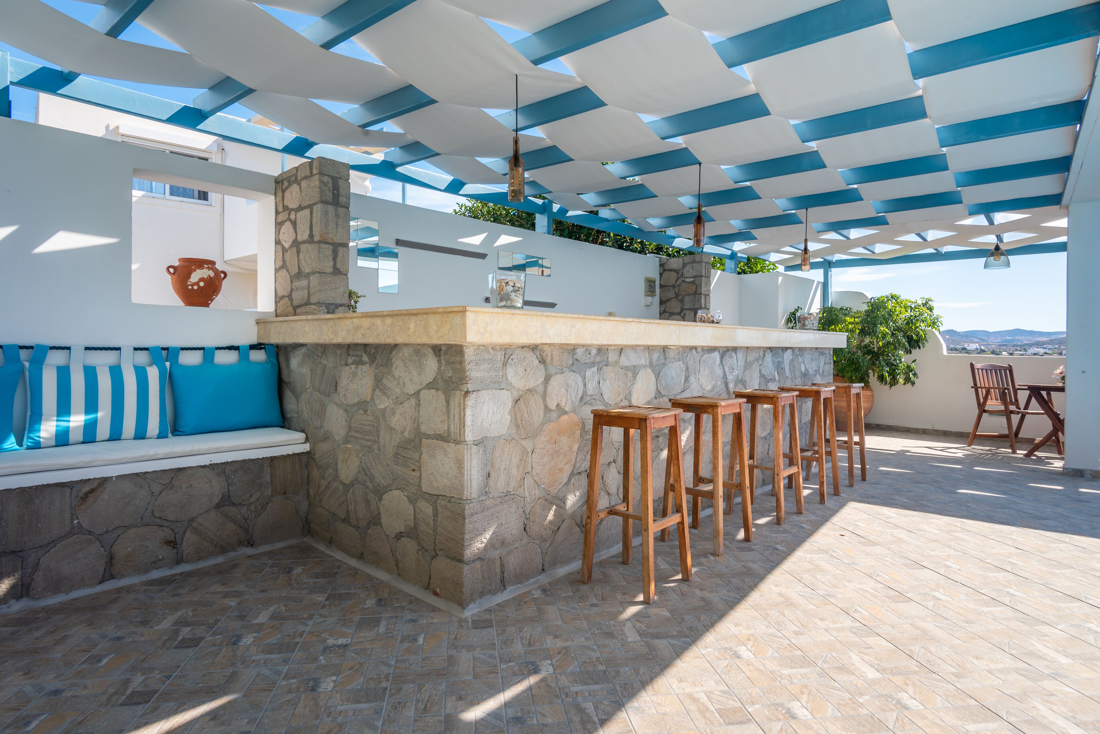 An outdoor bar area with stone walls, wooden stools, and a blue and white ceiling.