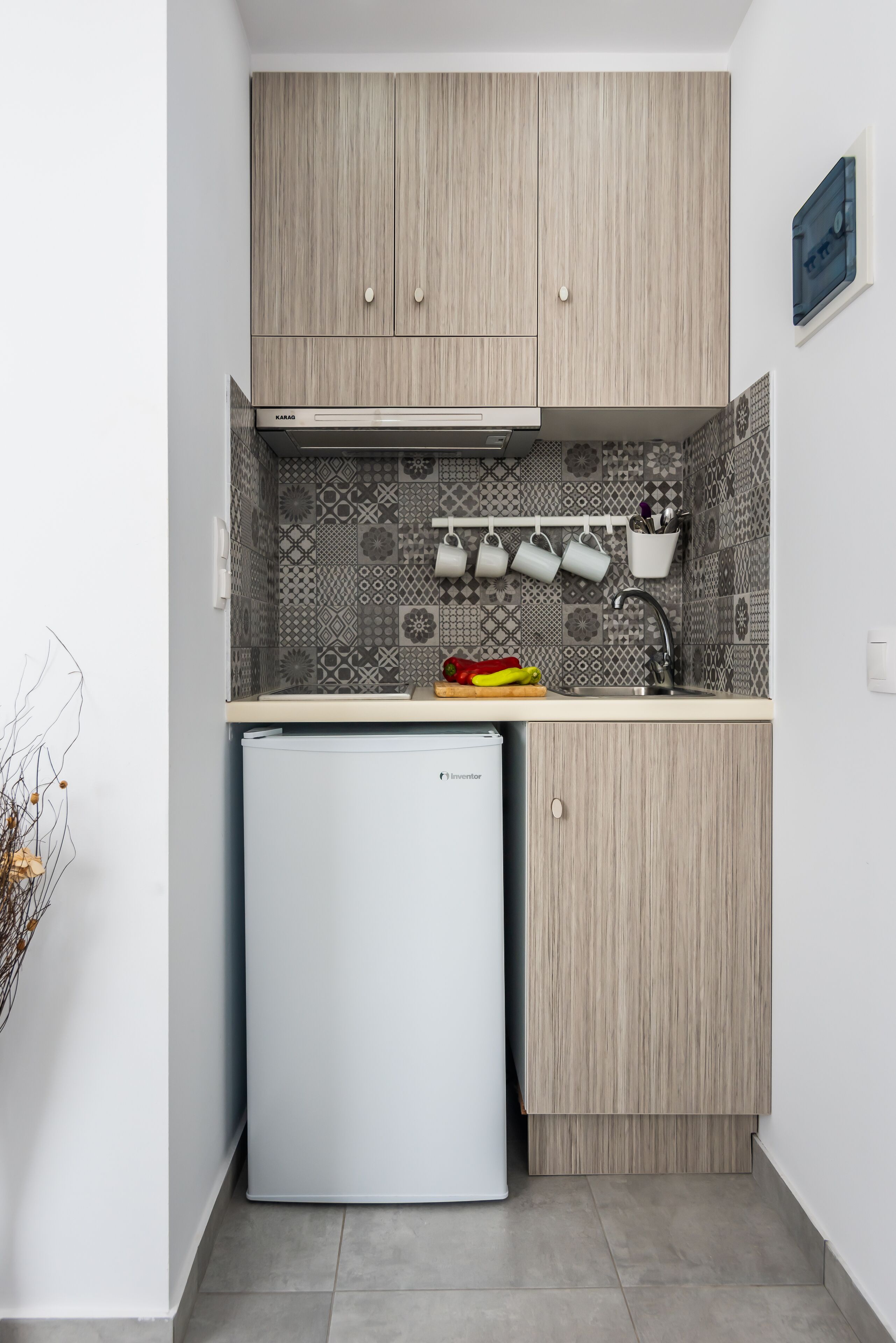 A compact kitchen with light wood cabinets, a patterned backsplash, and a small white refrigerator.