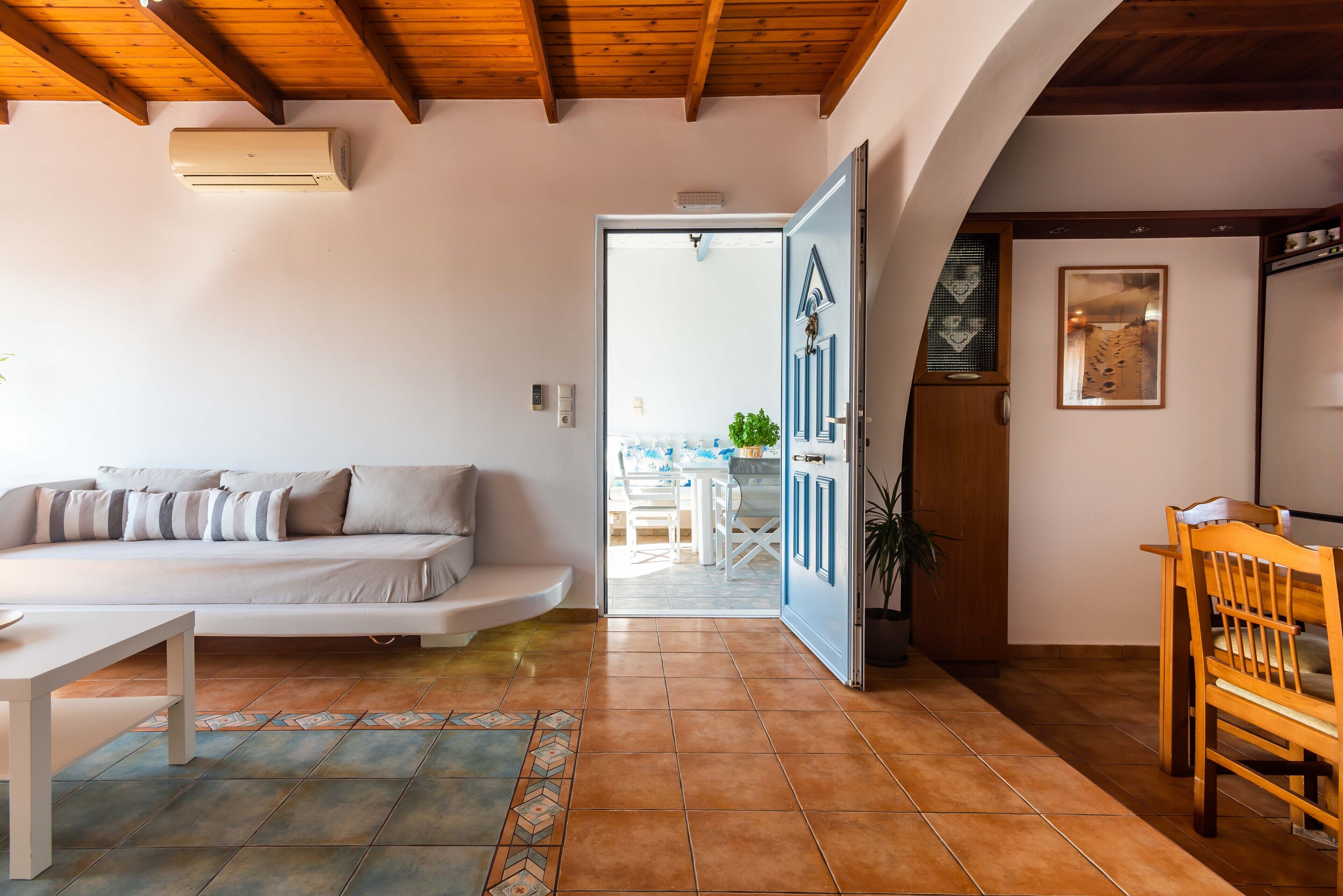 A living room with a sofa, a dining table, and a chair. There is a door leading to an outdoor area.