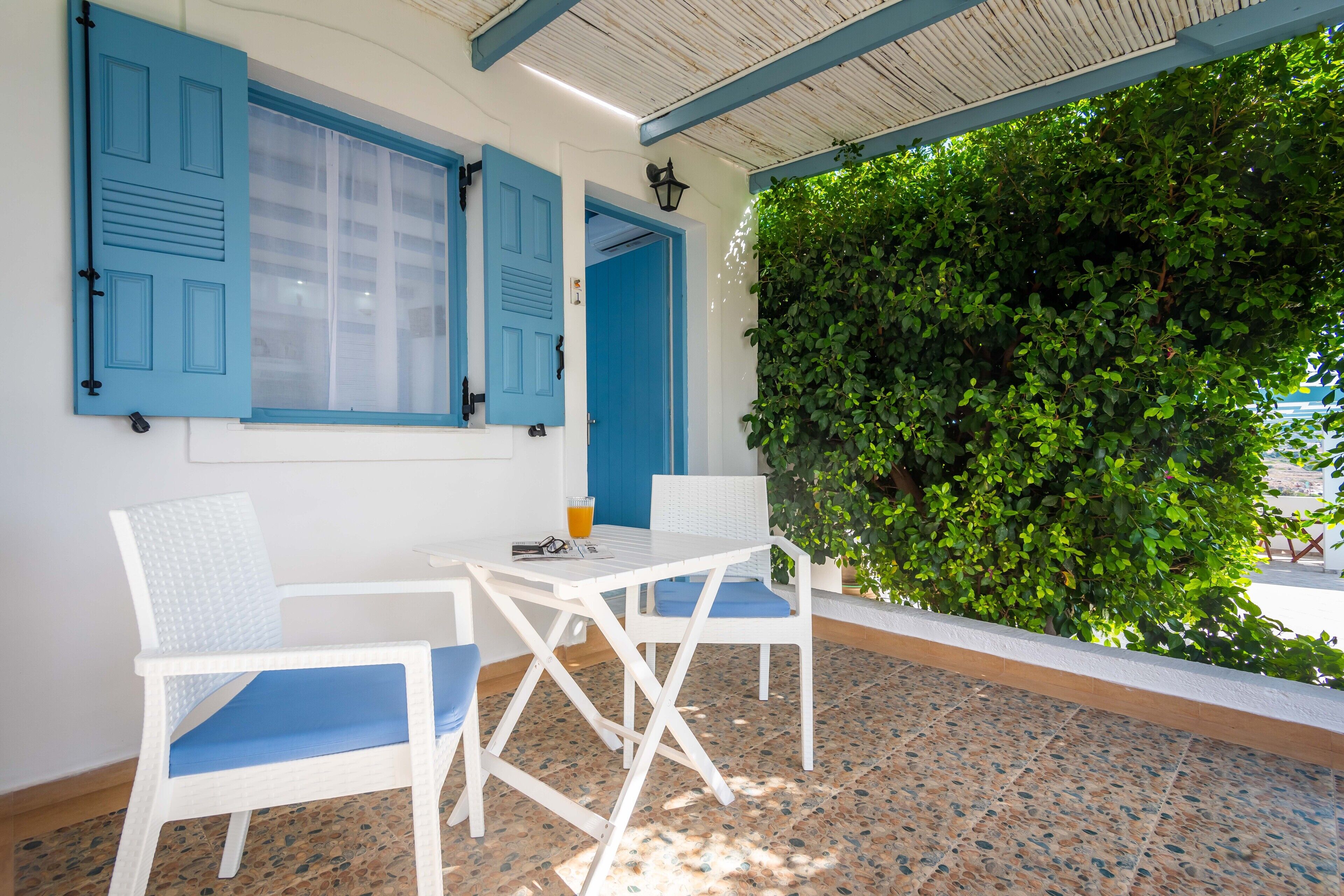 Une pièce avec une table blanche et deux chaises, une porte bleue et un mur végétal vert.