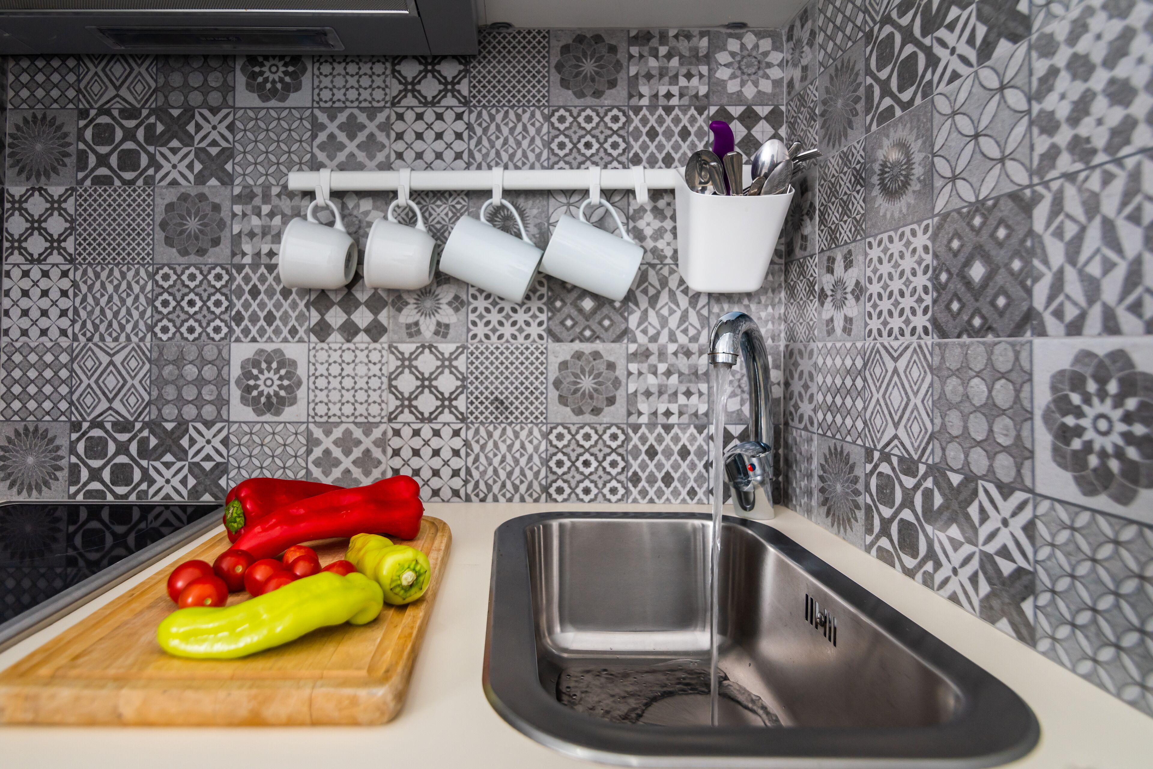 Una cocina con un lavamanos, una tabla de cortar con verduras y un organizador de utensilios en la pared.