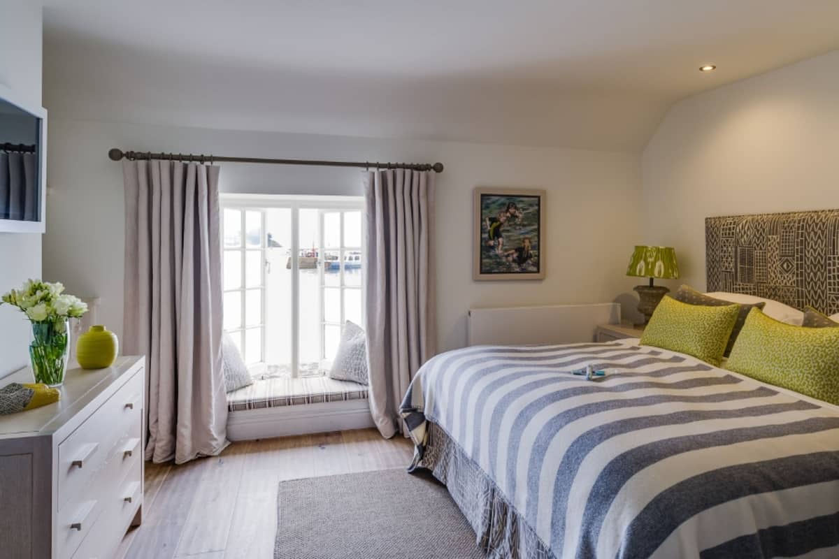 A bedroom with a bed, a window with curtains, a bedside table with a lamp, and a painting on the wall.