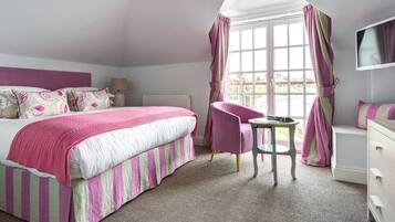 A bedroom with a bed, a chair, a table, a dresser, and a TV.