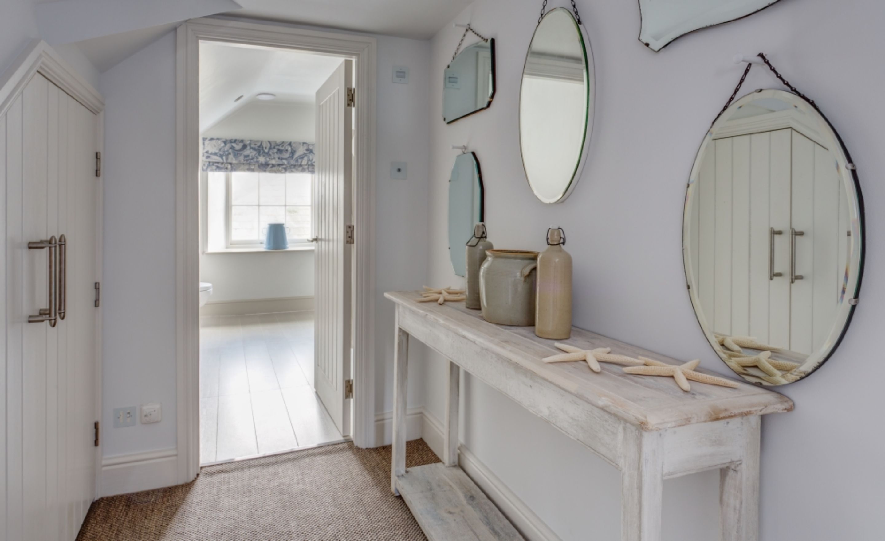 A hallway with a white door, a white console table with jars, and a mirror.