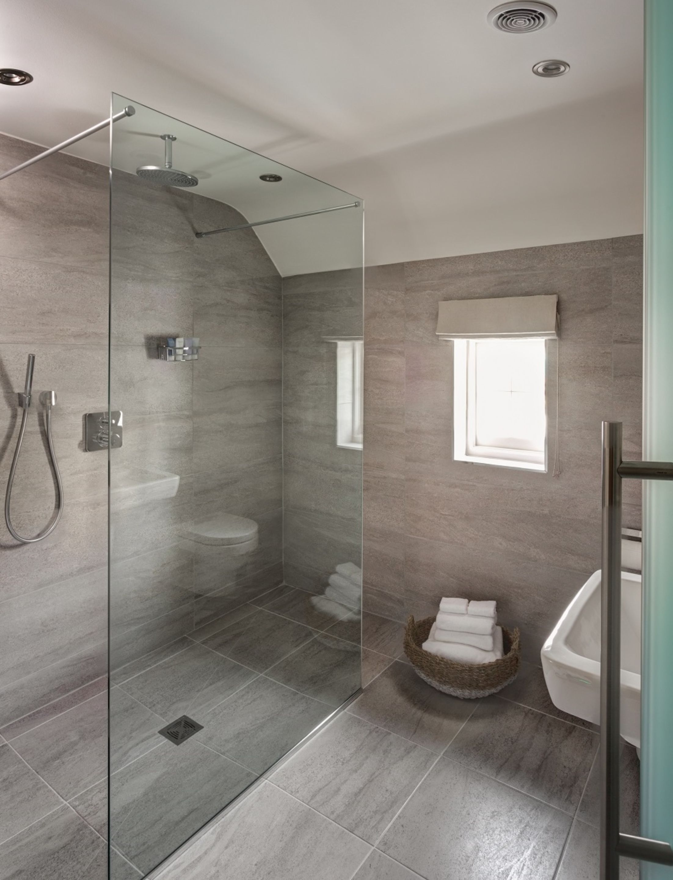 Een moderne badkamer met een douchecabine van glas, een toilet, een bad en een raam voor natuurlijk licht.