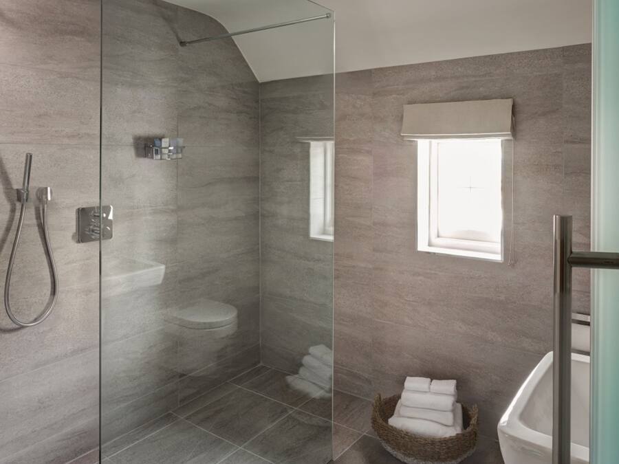Een moderne badkamer met een douchecabine van glas, een toilet, een bad en een raam voor natuurlijk licht.