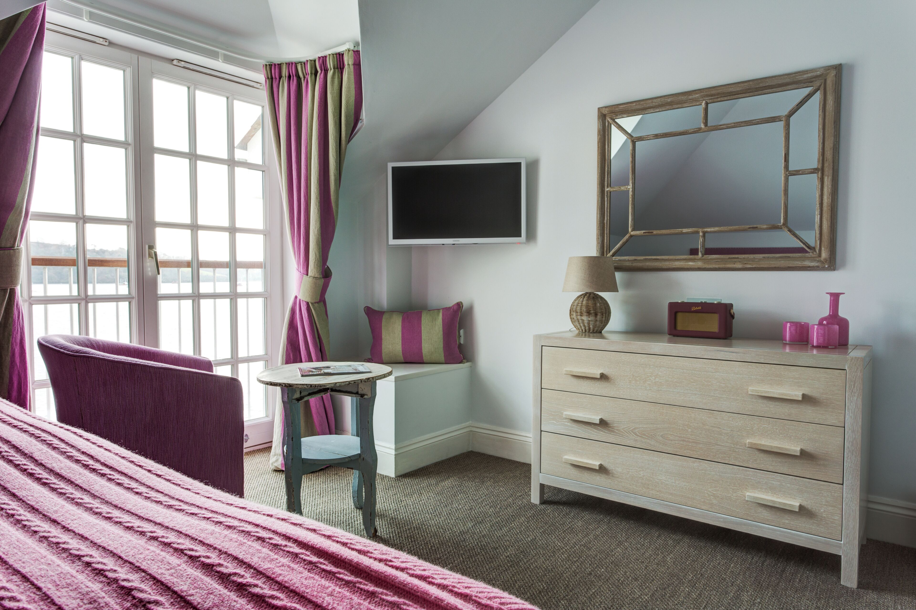 A bedroom with a bed, a chair, a desk, a dresser, a TV, and a window with curtains.