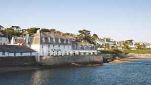 A coastal building with a stone wall, named "The Idle Rocks," adjacent to a body of water. - The Idle Rocks (Truro)
