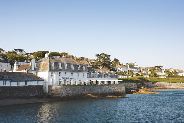 A coastal building with a stone wall, named "The Idle Rocks," adjacent to a body of water.