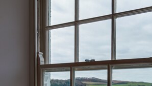 A room with a large window overlooking a body of water, a fur throw on the bed, and two pillows. - The Idle Rocks (Truro)