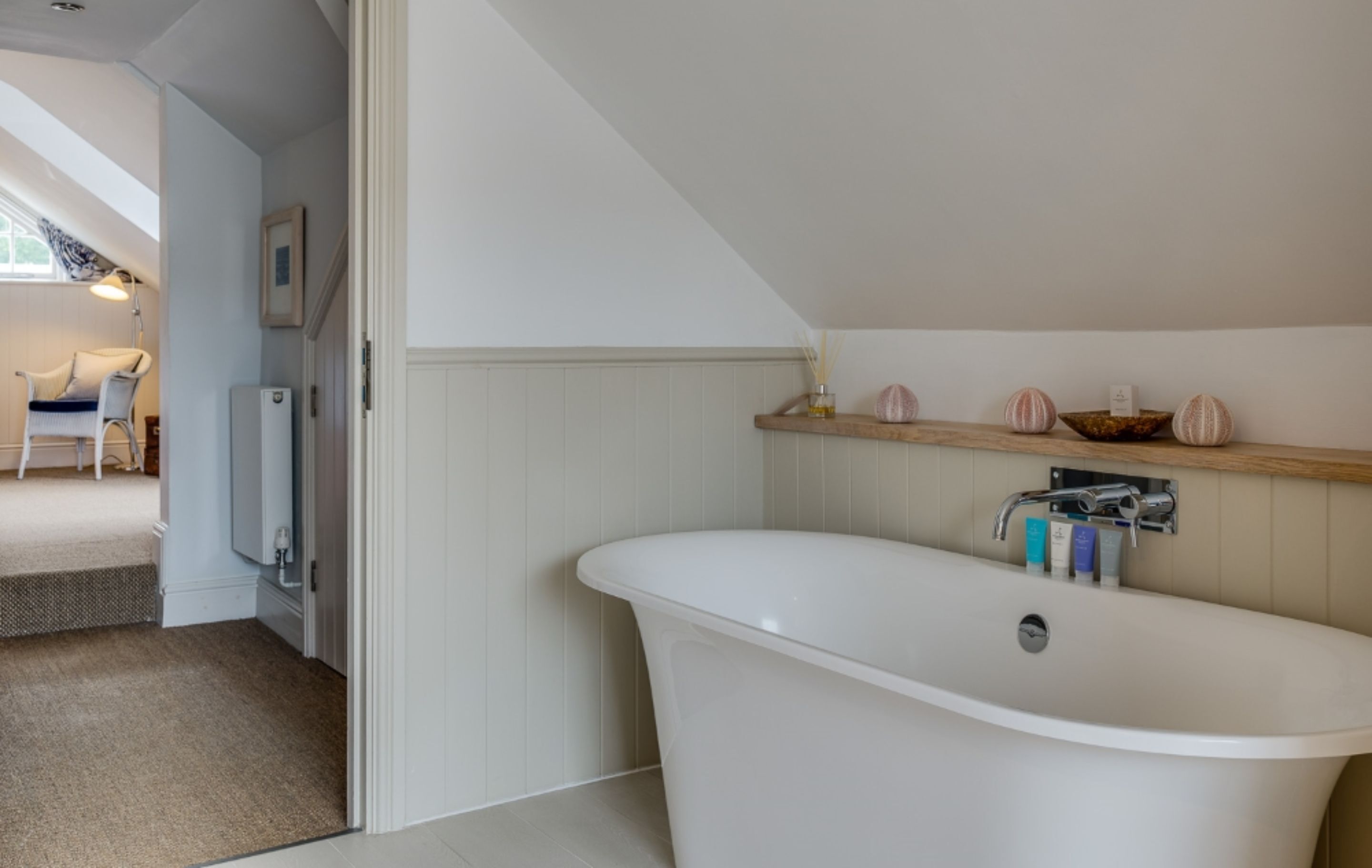Un baño moderno con una bañera independiente, un estante de madera con adornos y un cuadro en la pared.