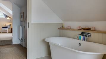 Un baño moderno con una bañera independiente, un estante de madera con adornos y un cuadro en la pared.