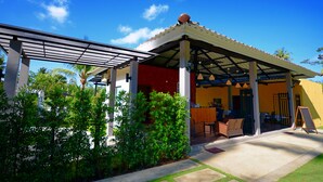 Un espacio de estar al aire libre cubierto con una pérgola, un mostrador de recepción y vistas de la vegetación circundante.