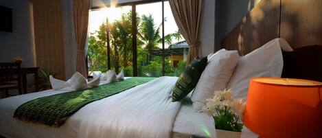 Habitación de hotel con una cama grande, una mesita de noche con lámpara y vistas a palmeras a través de la ventana.