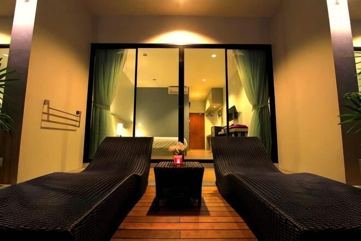 Une pièce comprenant deux fauteuils de relaxation en osier, une petite table et une porte-fenêtre coulissante donnant sur une chambre.