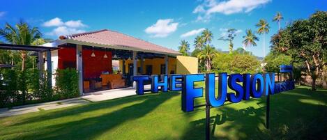 A resort named "The Fusion Resort" with a red building, outdoor seating, and palm trees.