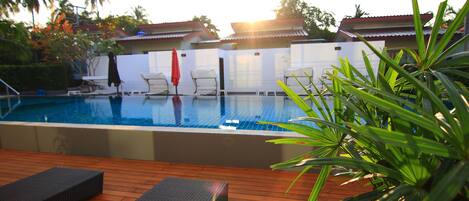 A pool area with lounge chairs, a wooden deck, and a view of the surrounding buildings.