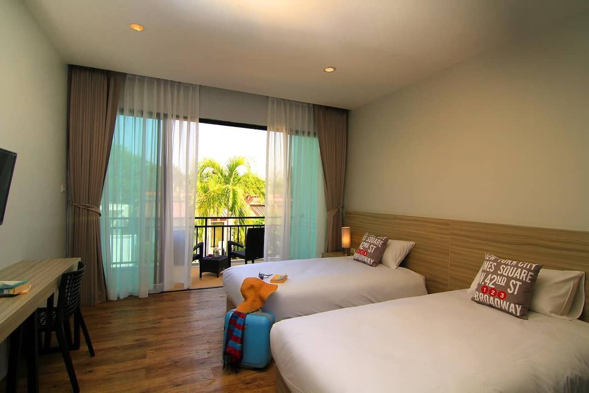 Une chambre d’hôtel avec deux lits, un bureau, une chaise et un balcon donnant sur des palmiers.
