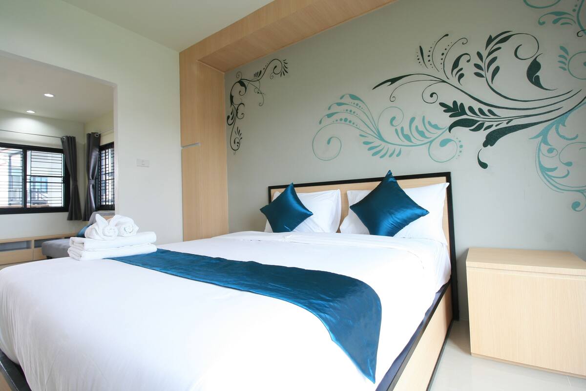 A neatly made bed with white and blue bedding, a wooden headboard, and a decorative wall mural.