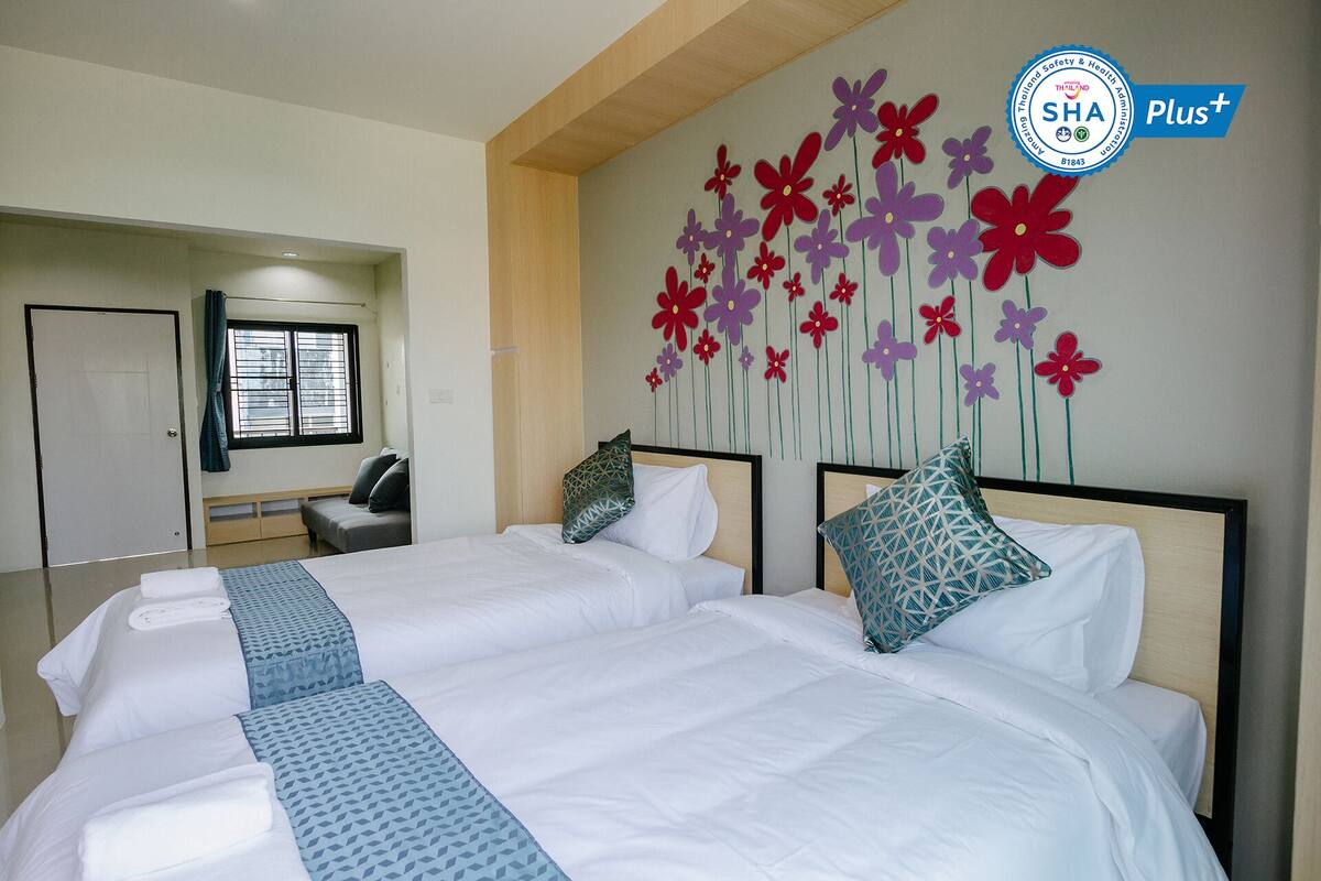 A hotel room with two beds, a wall decoration of flowers, a window with blinds, and a door.