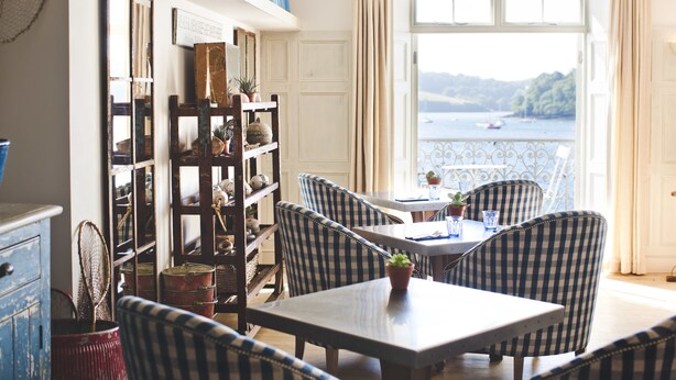 A dining area with checkered chairs, a table, and a view of the sea through a window. - St Mawes Hotel (Truro)