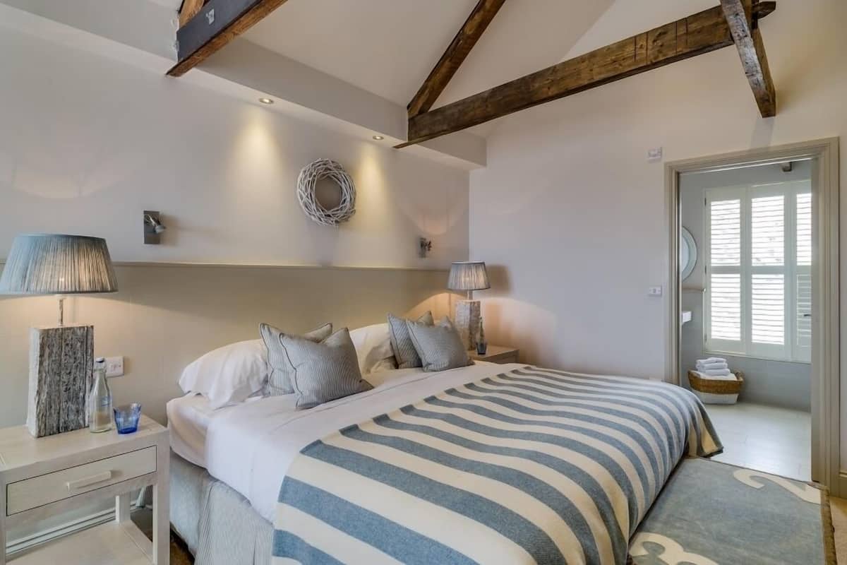 A bedroom with a large bed, two bedside tables, a lamp, a wall-mounted light, and a window with blinds.