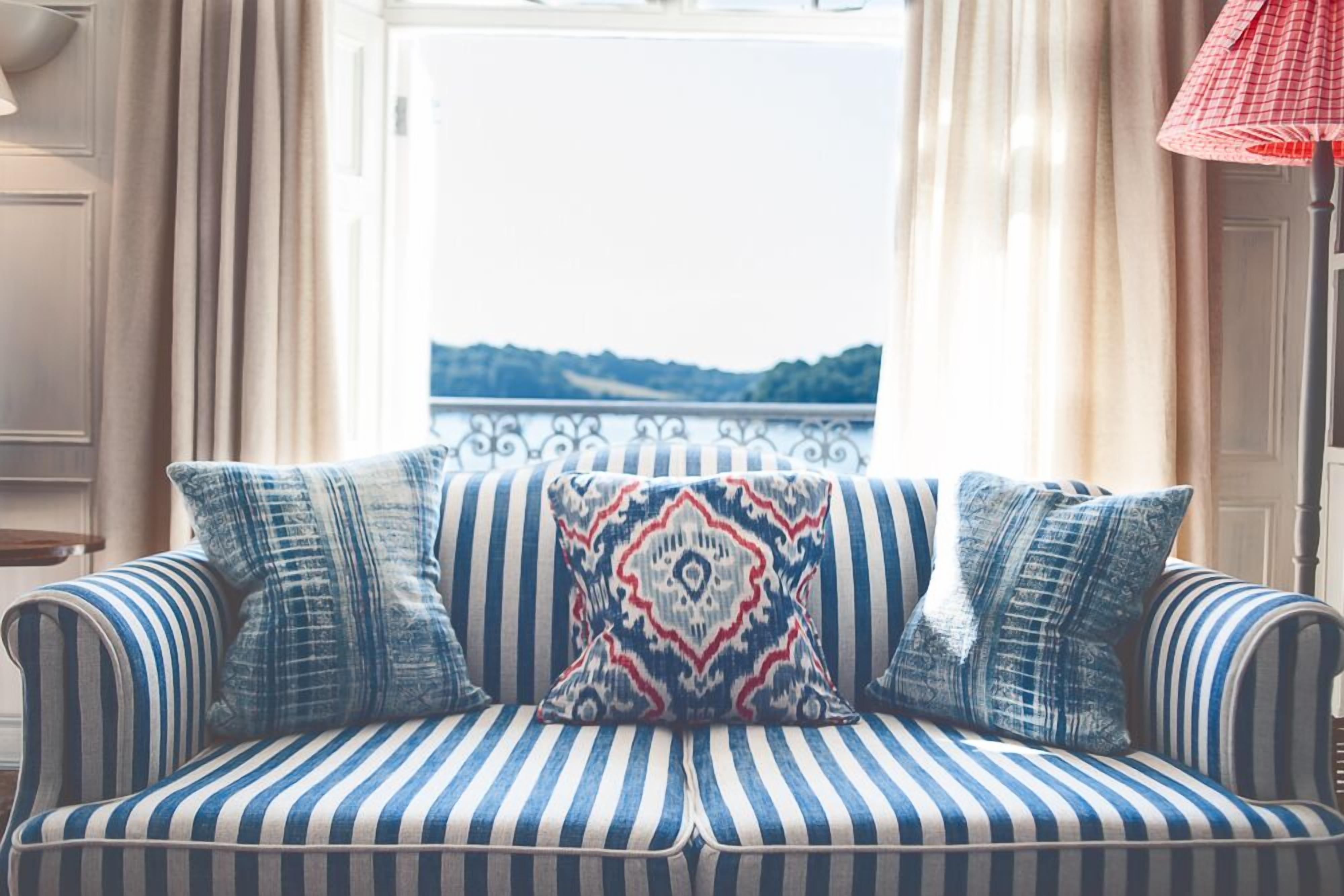 Un divano a righe con cuscini decorati in una stanza con vista su un paesaggio attraverso una finestra.