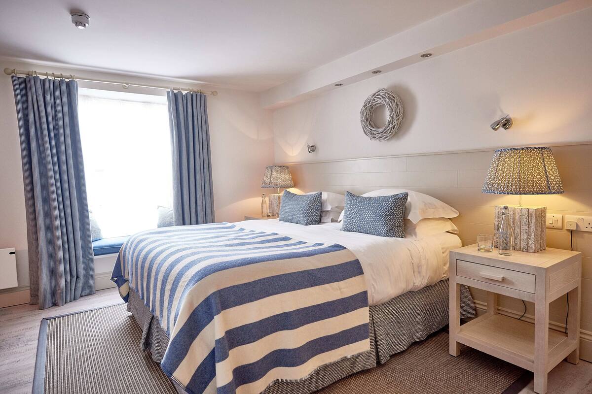 A bedroom with a bed, nightstands, a window with curtains, and a wall-mounted lamp.