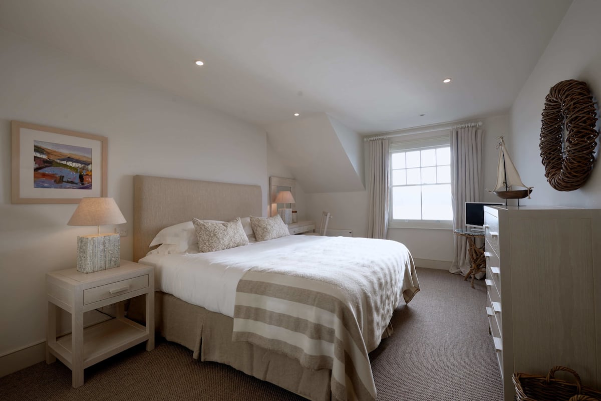 A bedroom with a large bed, bedside lamps, a TV, and a painting on the wall.