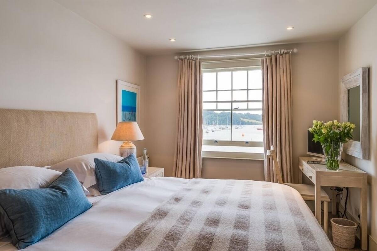 A hotel room with a large bed, a desk with a lamp, a TV, and a window with curtains.