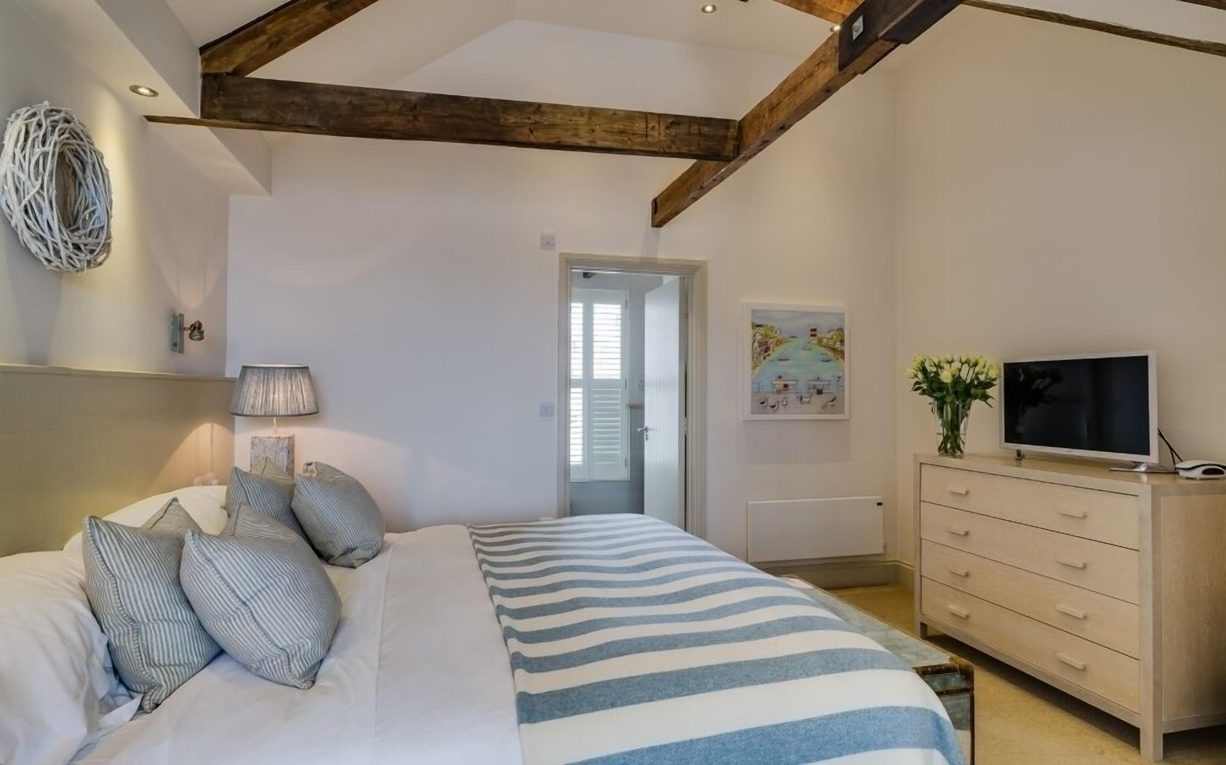 Un dormitorio con cama, cómoda, televisor y puerta que da a otra habitación.