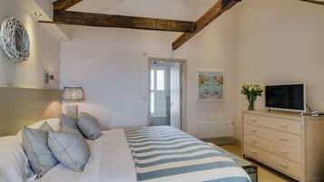 Un dormitorio con cama, cómoda, televisor y puerta que da a otra habitación.