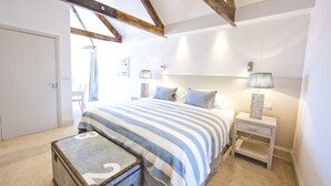 A bedroom with a large bed, a nightstand, a lamp, a suitcase, and a door. - St Mawes Hotel (Truro)